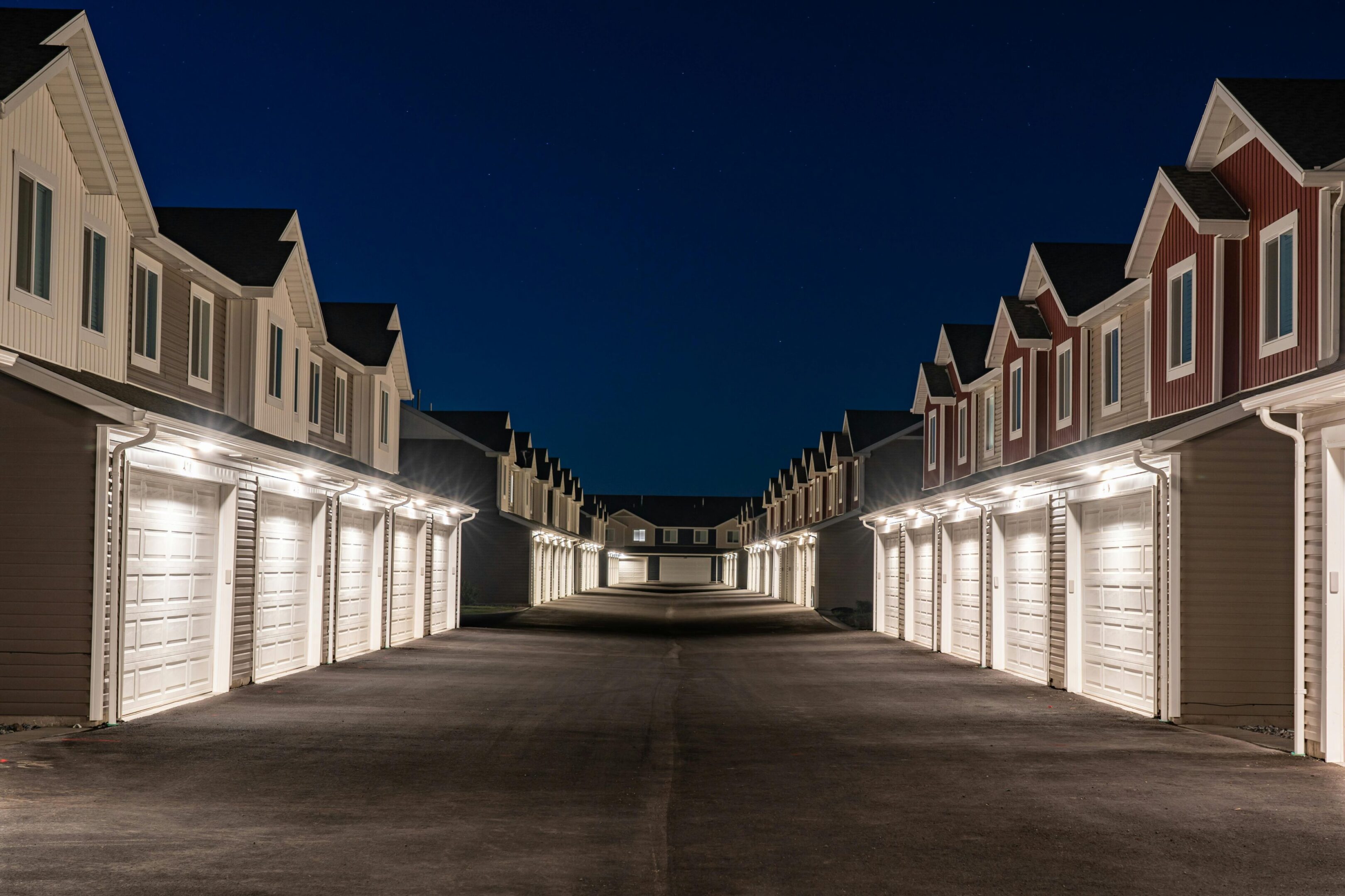 Row of illuminated garages lining a residential street at night.